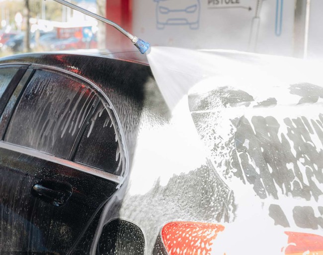 Car being washed with a high-pressure water jet at PUTO self-service car wash.