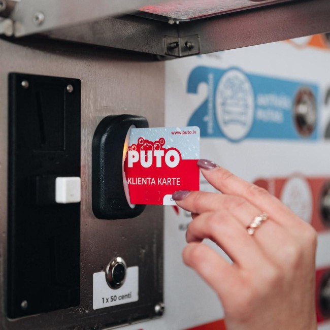 Hand holding a PUTO client card at a payment machine sensor.