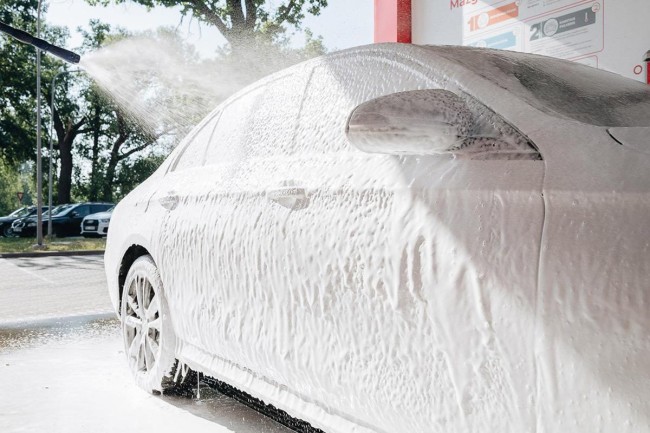 Car at the PUTO car wash, covered in foam and being washed with a high-pressure water spray.