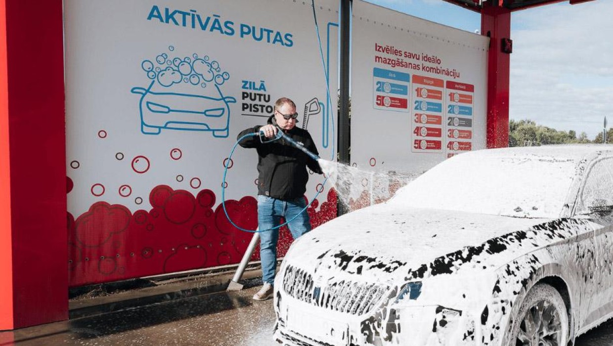 Vīrietis mazgā auto ar putām PUTO pašapkalpošanās automazgātavā.