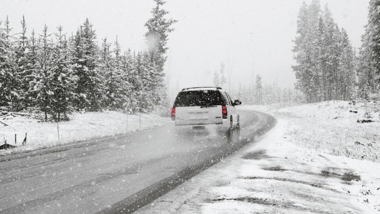 Auto ziemas ceļā sniegotā mežā, atstājot sniega pēdas un izraisot sniegputeni.