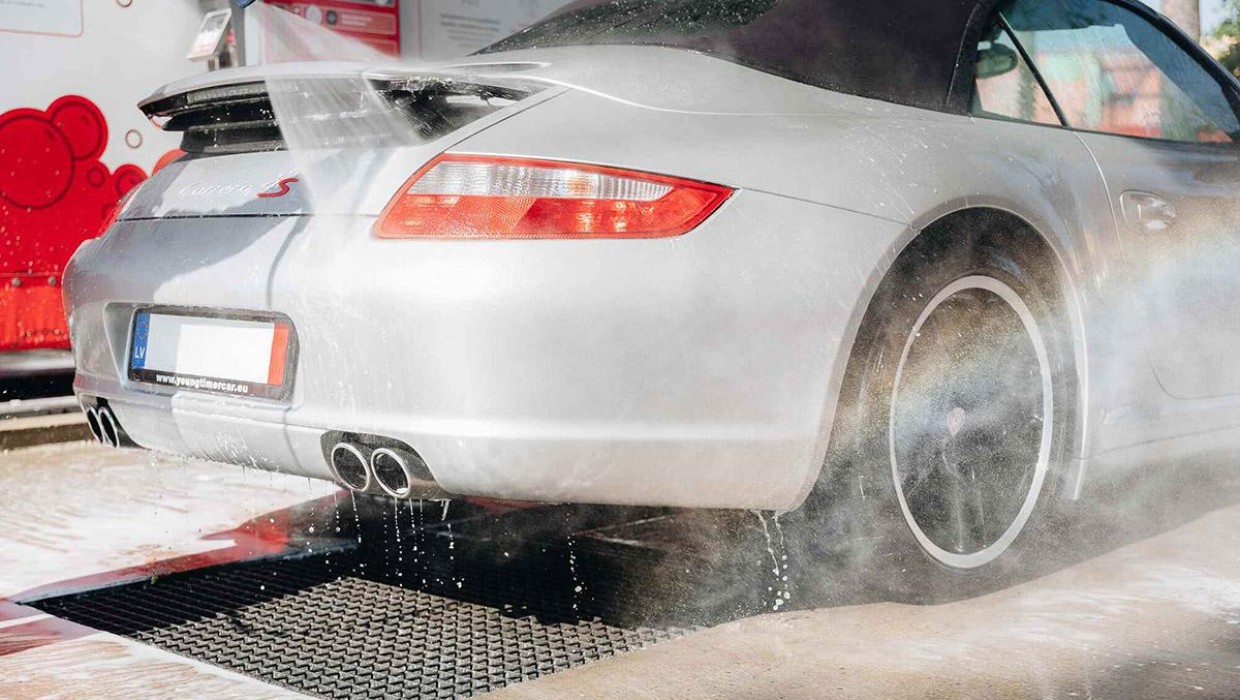 Car being washed with a high-pressure washer at PUTO self-service car wash during summer.