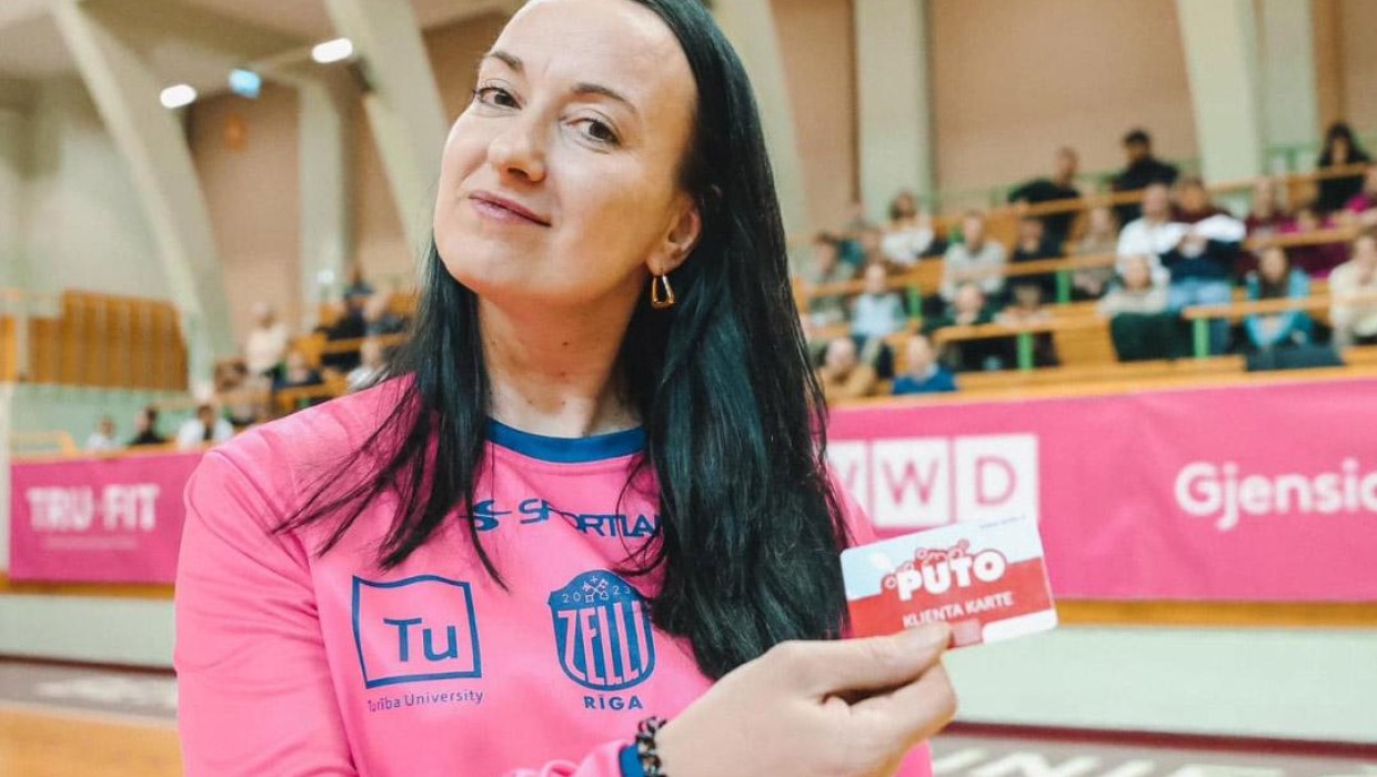 A woman holding a PUTO client card at a basketball game with Rīgas Zeļļi.