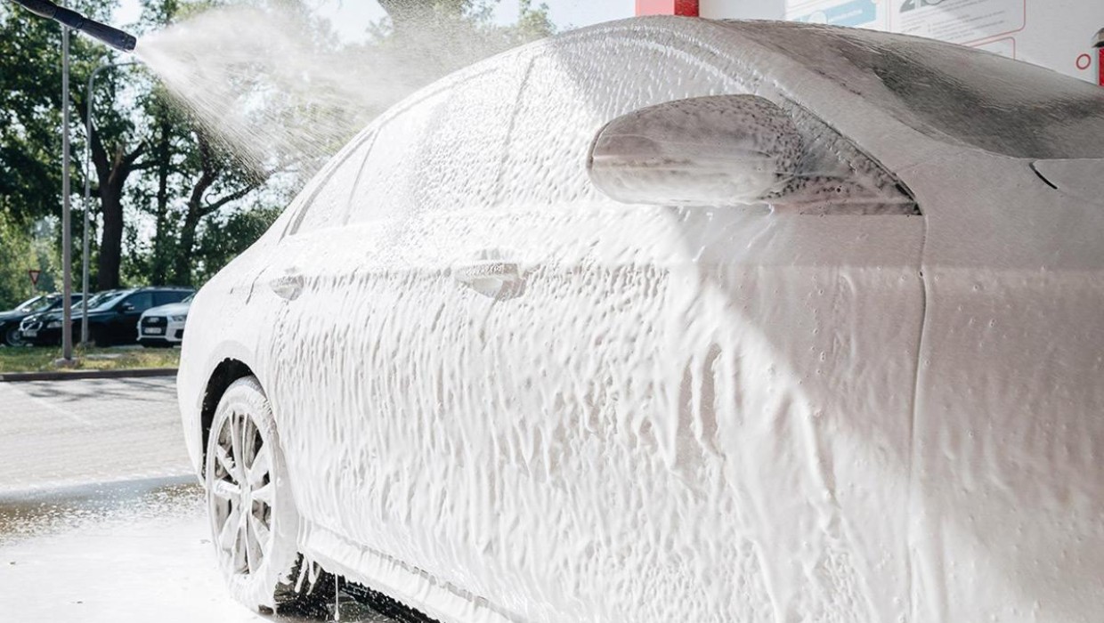 Car at the PUTO car wash, covered in foam and being washed with a high-pressure water spray.